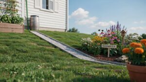 A white house with a green downspout feeding into a silver rain barrel sits on a green, grassy slope, with a stone-lined channel extending downhill fr
